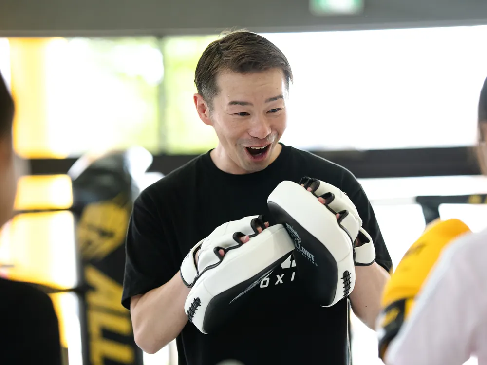 会員のミットを受けながら笑顔で指導する華井マネージャー